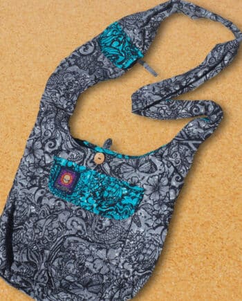 cotton beach bag with many zip pockets and a clever phone pocket on the wide shoulder strap. printed with a tattoo design in black on a grey background and contrasting jade pocket flaps