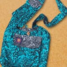 cotton beach bag with many zip pockets and a clever phone pocket on the wide shoulder strap. printed with a tattoo design in black on a jade green background and contrasting grey pocket flaps