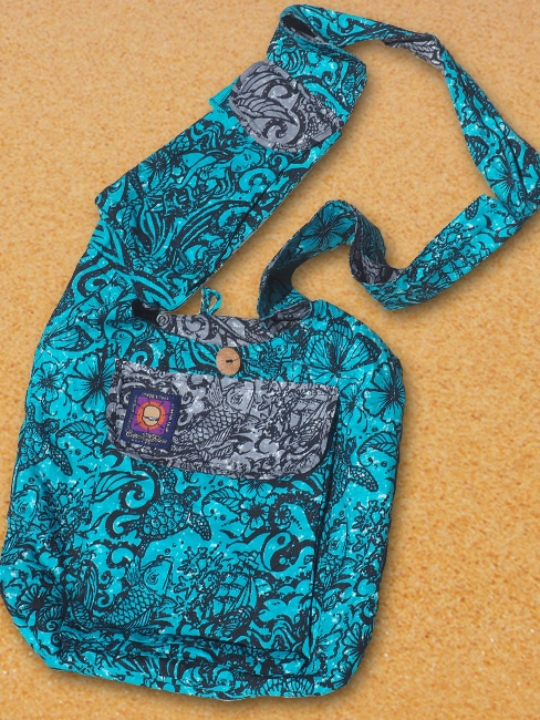 cotton beach bag with many zip pockets and a clever phone pocket on the wide shoulder strap. printed with a tattoo design in black on a jade green background and contrasting grey pocket flaps